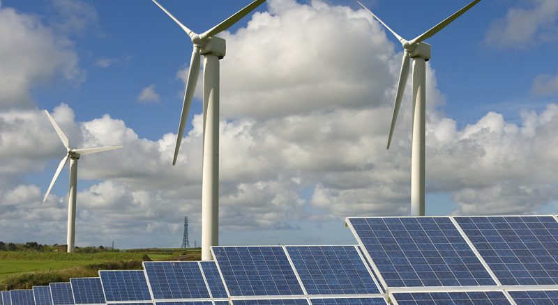 Grünes Feld mit Windturbinen und Solaranlagen unter bewölktem und blauem Himmel