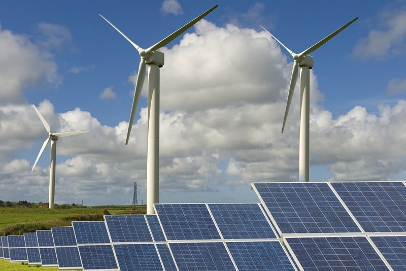 Grünes Feld mit Windturbinen und Solaranlagen unter bewölktem und blauem Himmel